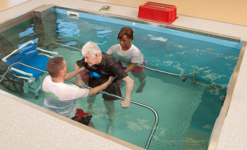 Trainers helping a person train in pool